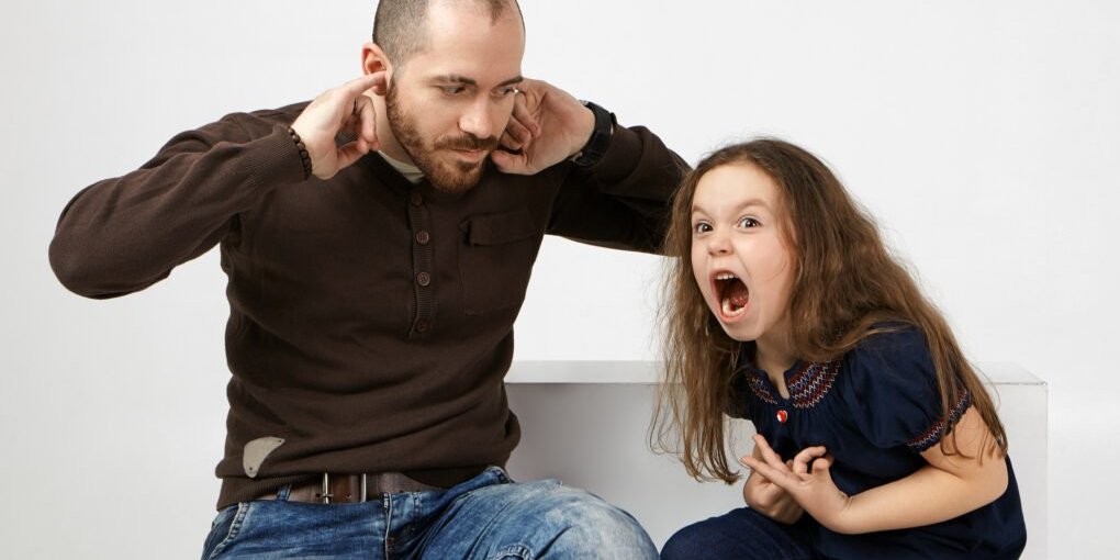 Vater hält sich die Ohren zu, während ein Kind neben ihm laut ruft