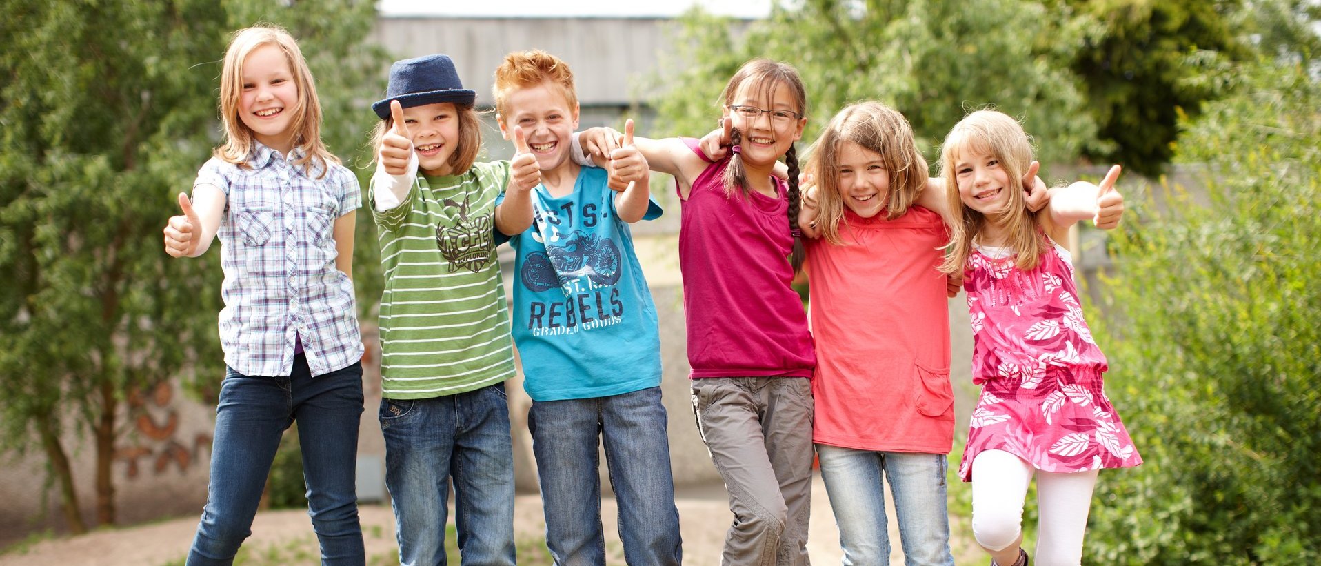 Sechs Kinder stehen gemeinsam im Freien und zeigen lächelnd den Daumen nach oben