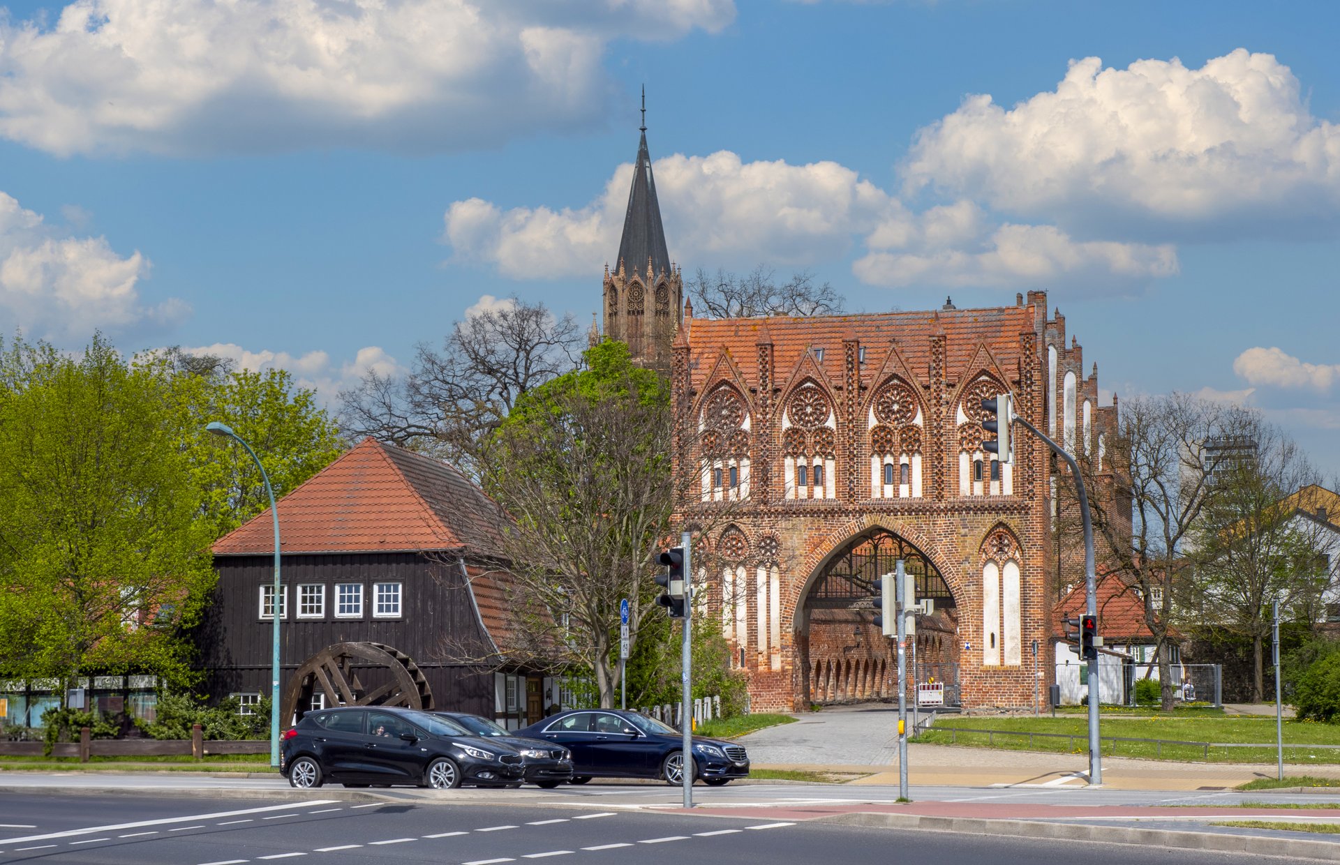 Historisches Backsteingebäude mit Turm an einer Straße unter blauem Himmel.